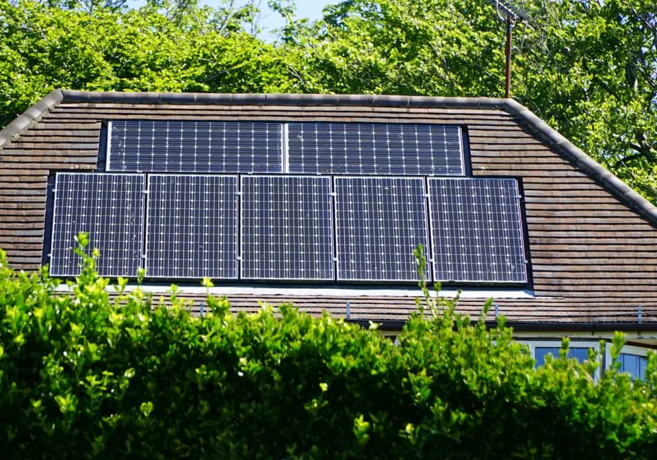 Solceller på et tegltag bag en hæk